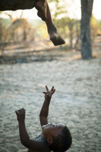 Reaching for a Foot The older children in this bushman village spent a lot of time climbing and sitting along a low branch of the biggest tree. This little boy was too young to climb up so he had his fun trying to catch the feet dangling down. Nhoma, Namibia.
